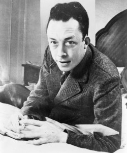 Albert_Camus,_gagnant_de_prix_Nobel,_portrait_en_buste,_posé_au_bureau,_faisant_face_à_gauche,_cigarette_de_tabagisme